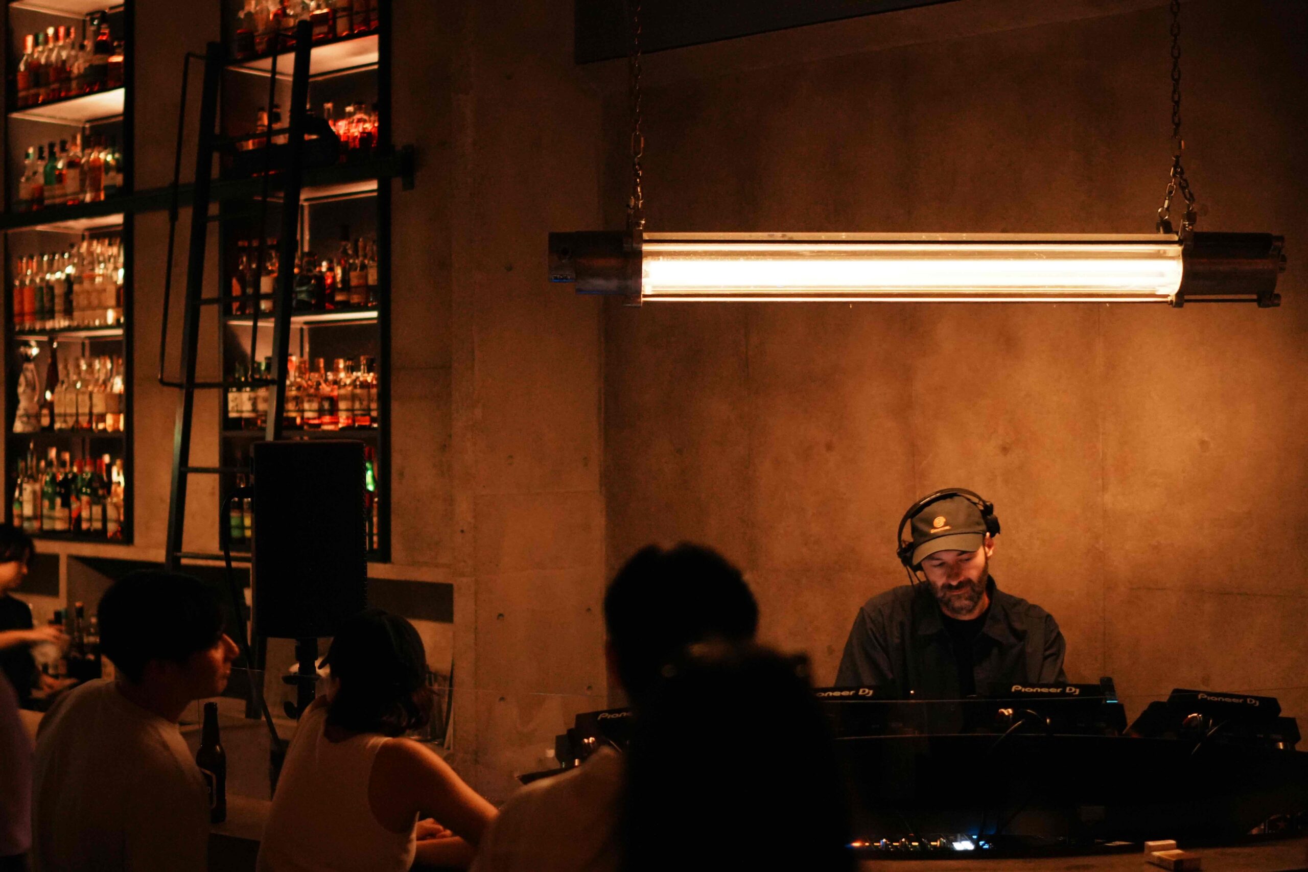 LVCA of Sabotage Milano performing a DJ set in a dimly lit bar, photographed by Raphael Borges.